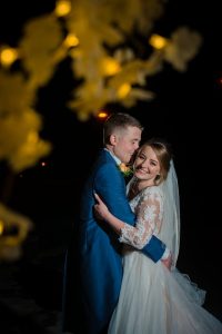 bride and groom laugh under trees at night