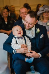 baby laughs at wedding ceremony sitting on dad's knee