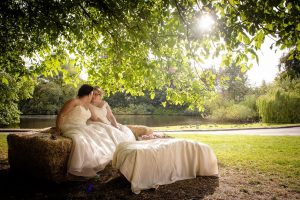 brides cuddle under large willow tree in the sunlight