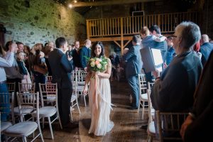bride comes down aisle in barn wedding