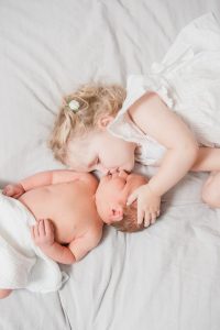 newborn boy gets a kiss from big sister