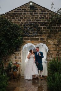 newlyweds outside Chilli Barn wedding venue in the rain with umbrellas