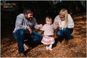 mum and dad helping toddler to walk in the woods