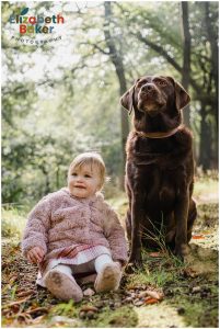 baby in fur coat sits with a chocolate brown labrador
