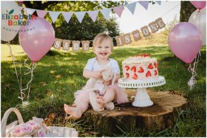 baby on first birthday with bunting and balloons cake smash