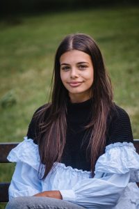 brown haired girl smiling sitting on bench outdoors looking at the camera