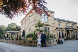 newlywed couple sitting on wall at Manor House landscape view