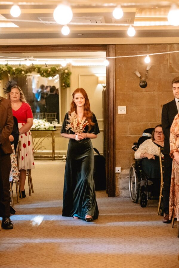 bridesmaid comes down the aisle in a green velvet dress