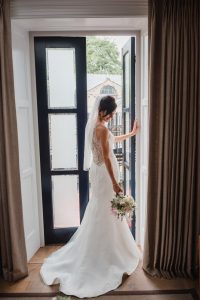 bride stands by open door looking back into the room at her flowers at Manor House