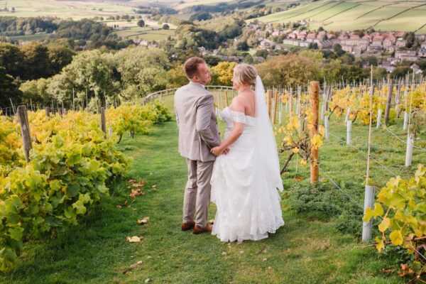 the newlywed bride and groom look at each other with rolling hills and vines growing in the background at Holmfirth Vineyard
