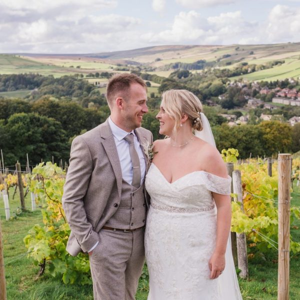 the newlywed bride and groom look at each other with rolling hills and vines growing in the background at Holmfirth Vineyard