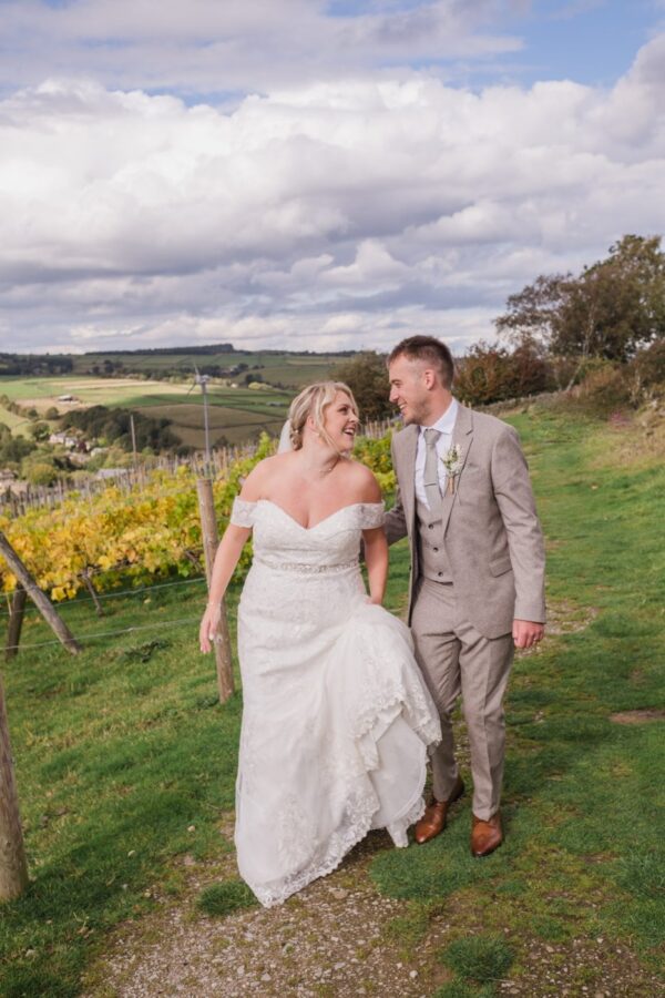 the newlywed bride and groom look at each other with rolling hills and vines growing in the background at Holmfirth Vineyard
