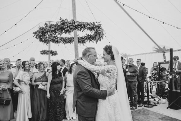 black and white image of newlyweds dancing in a marquee with guests watching on.